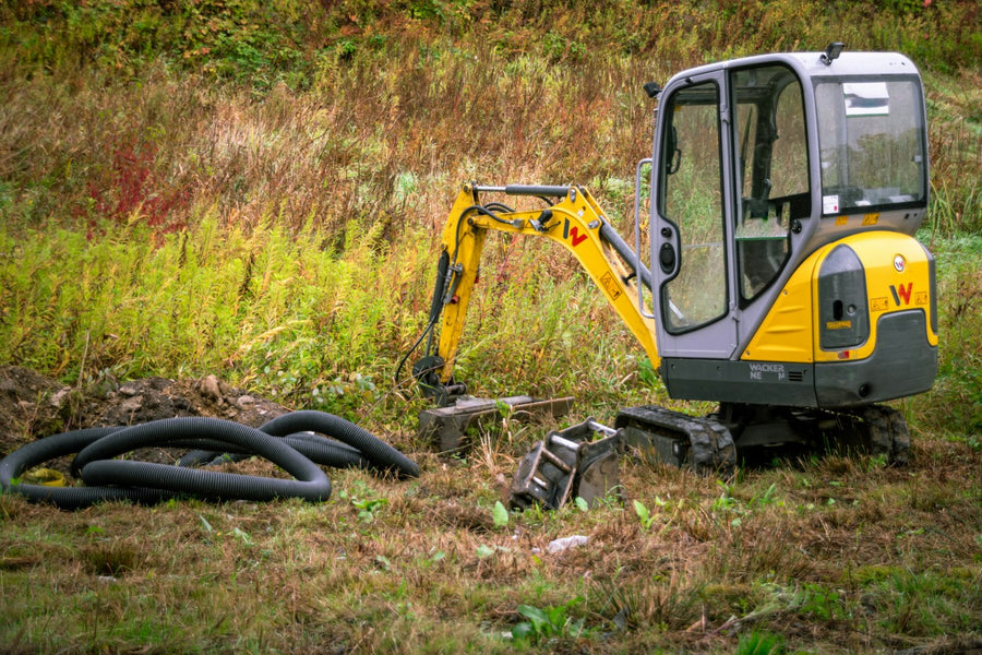 Mini excavator beside coiled drainage pipe on a grass site